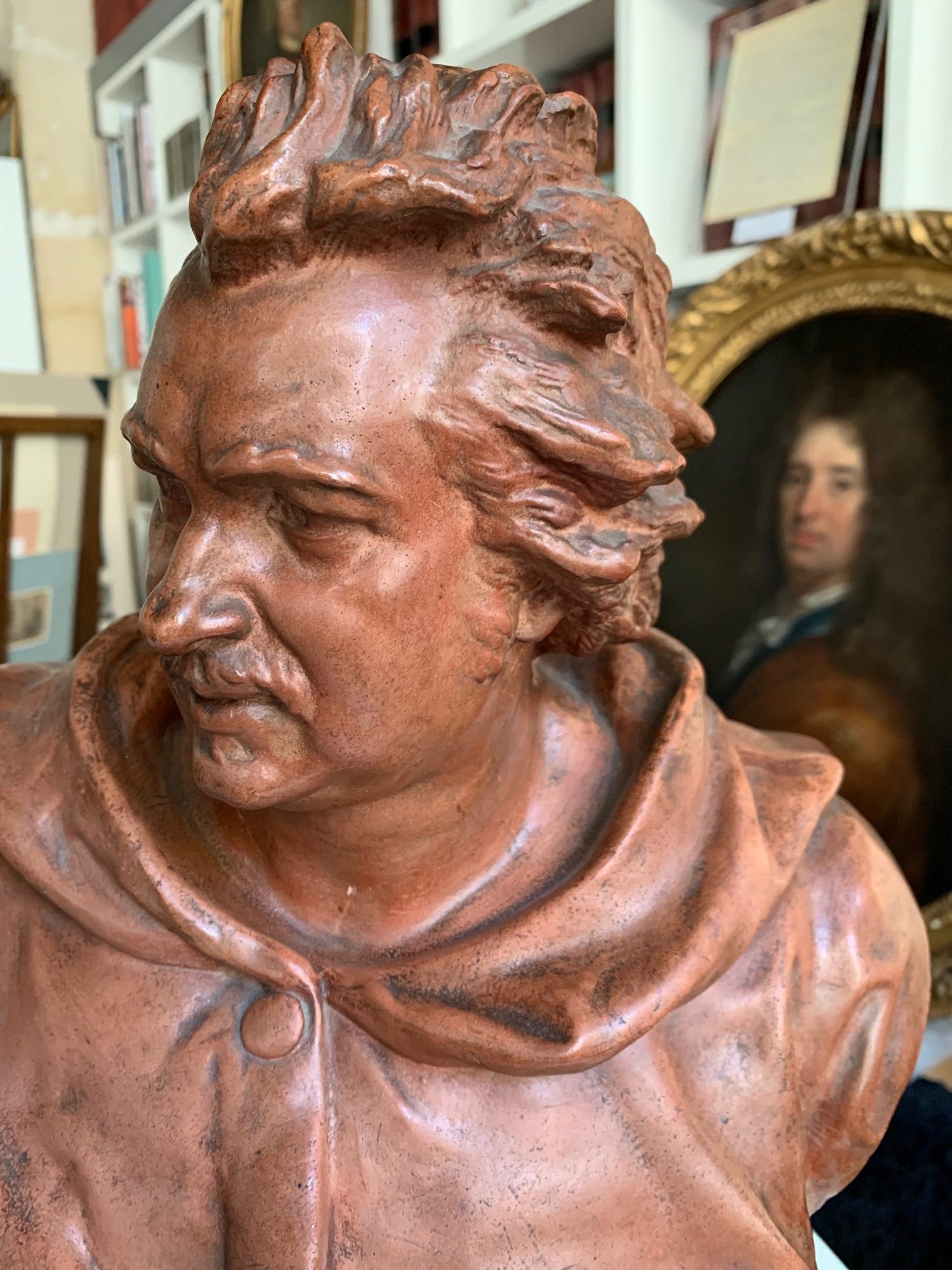 Busto de terracota de un escritor con túnica con capucha frente a un retrato antiguo